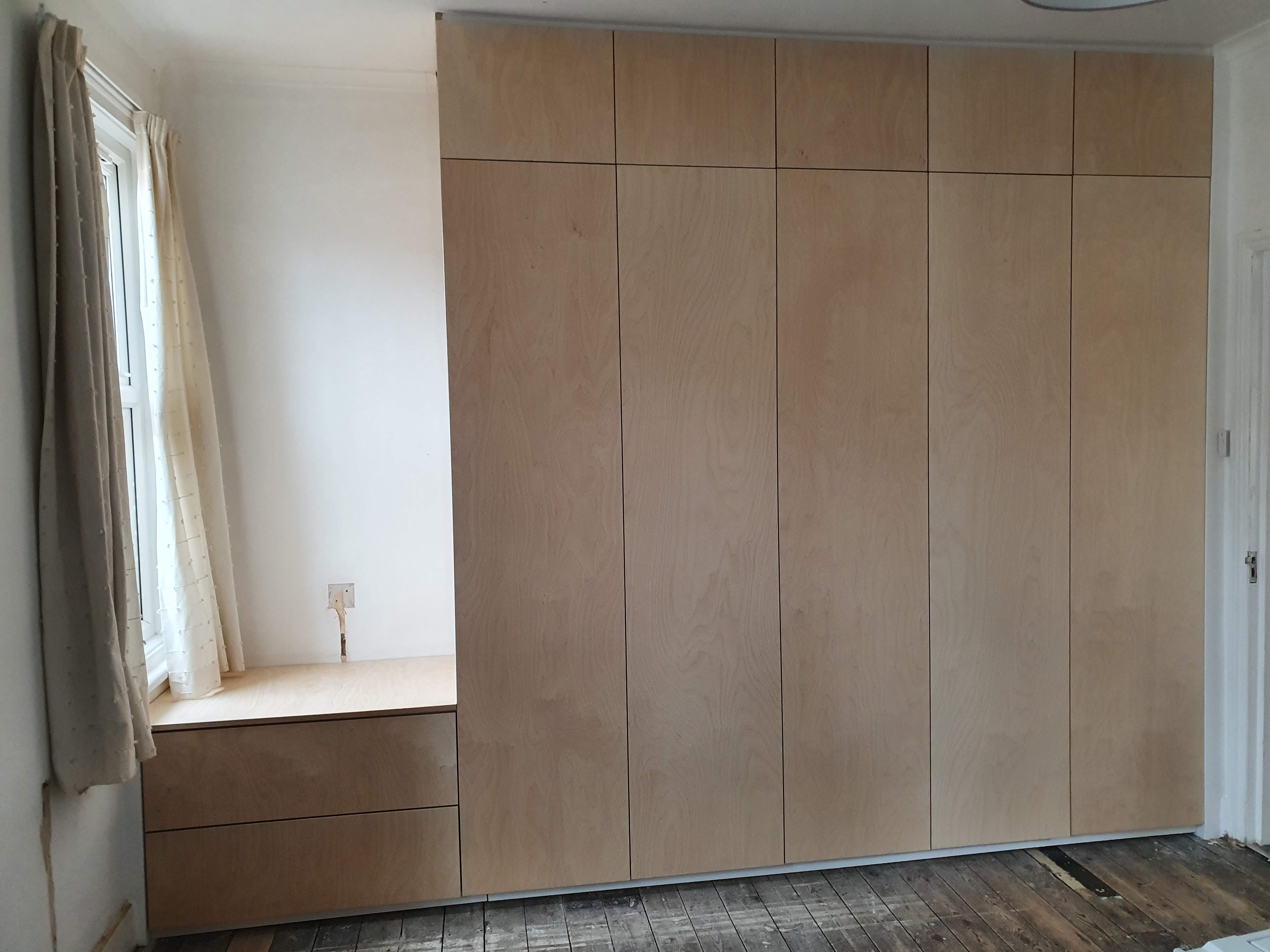 Minimalist fitted wardrobe in natural plywood with push-to-open doors